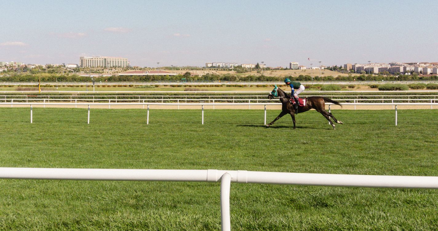 Jockey seul au galop sur une piste en herbe, vue d'ensemble de l'hippodrome