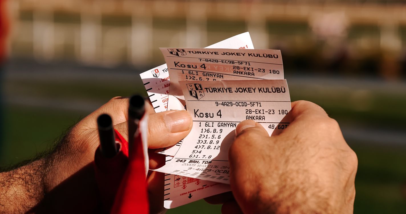 Tickets de paris hippiques tenus en main, hippodrome flouté en arrière-plan